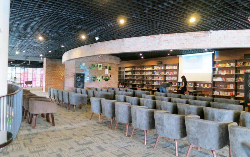 cafe-sach-ha-noi-5 Phòng hội thảo với ghế xếp thành hàng, kệ sách phía sau, và màn hình chiếu trên tường.