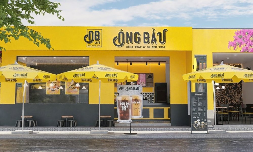 Khám Phá 10+ Quán Cafe Đẹp Nhất Long Biên: Thỏa Sức “Sống Ảo”, Thưởng Thức Đồ Uống Ngon 7 Mặt tiền quán cà phê màu vàng sáng, có nhiều ô dù che và biển hiệu lớn trên tường.