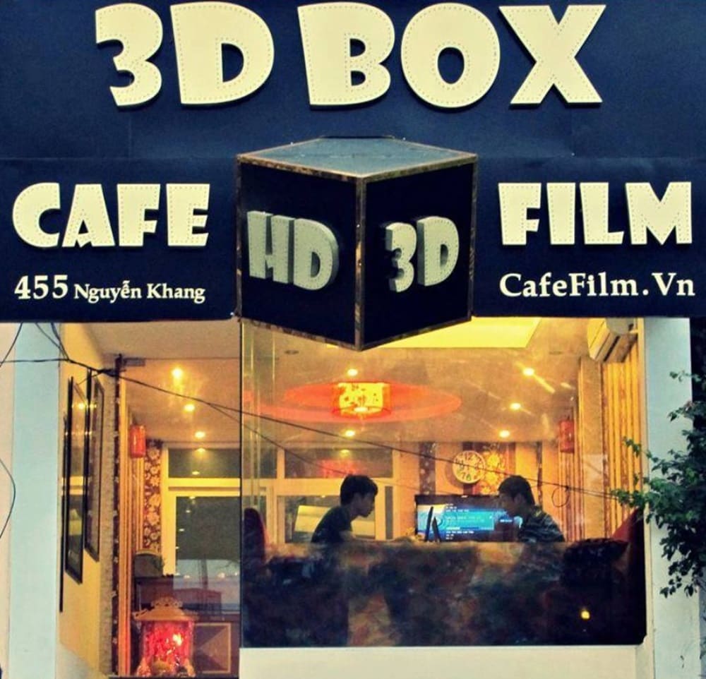 Top 9 Quán Cafe Phim Cầu Giấy Đáng Thử: Thưởng Thức Phim Hay, Cà Phê Ngon 14 Mặt tiền quán cà phê với biển hiệu "3D BOX" và hai người ngồi bên trong, ánh sáng ấm áp.