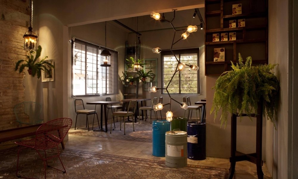 Khám Phá 15 Quán Cafe Yên Tĩnh ở Quận 1: Không Gian Thoải Mái, Thức Uống Tuyệt Hảo 15 Quán cà phê ấm cúng với đèn treo sáng, cây xanh trang trí và bàn ghế gỗ đơn giản.