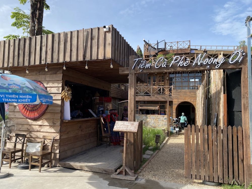 Khám Phá Top 10 Quán Cafe Sân Vườn Đẹp và Thư Giãn Tại Thủ Đức 7 Quán cà phê với thiết kế gỗ, có bảng hiệu và ô che nắng xanh, một người đi vào bên trong.