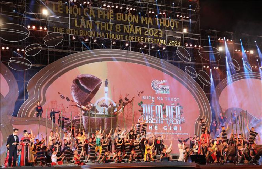 Sân khấu lễ hội với nhiều người biểu diễn và trang trí ánh sáng rực rỡ, có bảng hiệu sự kiện phía sau.