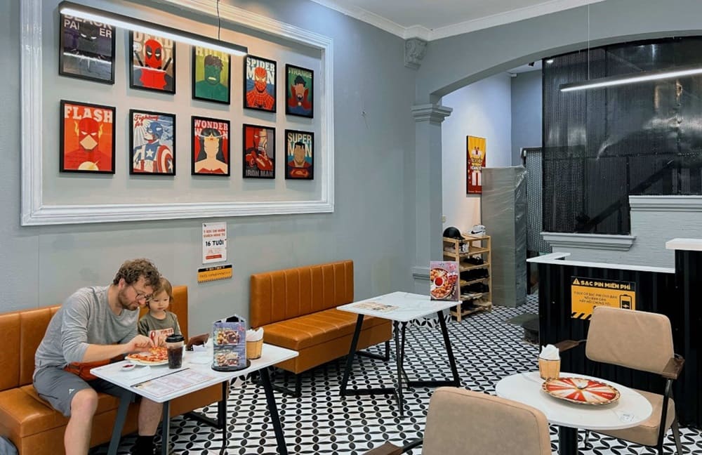 Top 9 Quán Cafe Phim Cầu Giấy Đáng Thử: Thưởng Thức Phim Hay, Cà Phê Ngon 10 Quán cà phê với tranh siêu anh hùng trên tường, bố trí bàn ghế kiểu hiện đại, có khách đang ngồi ăn.