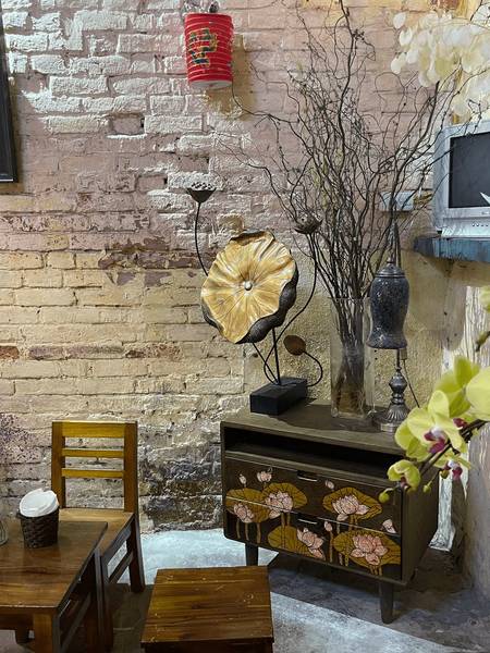 G&oacute;c ph&ograve;ng với b&agrave;n ghế gỗ, tủ trang tr&iacute; hoa sen, đ&egrave;n lồng đỏ treo, v&agrave; c&agrave;nh c&acirc;y kh&ocirc; trang tr&iacute; tr&ecirc;n nền tường gạch.