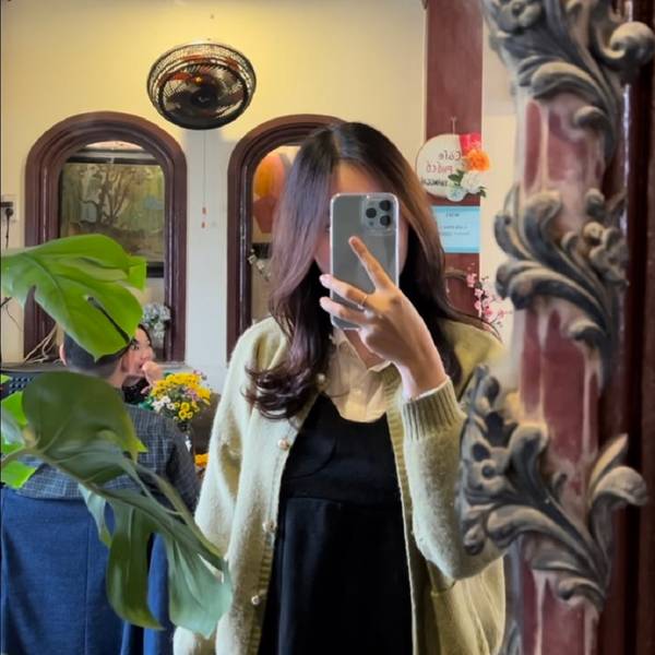 Người phụ nữ chụp ảnh tự sướng trước gương trong căn ph&ograve;ng trang tr&iacute; với c&acirc;y xanh v&agrave; hoa.