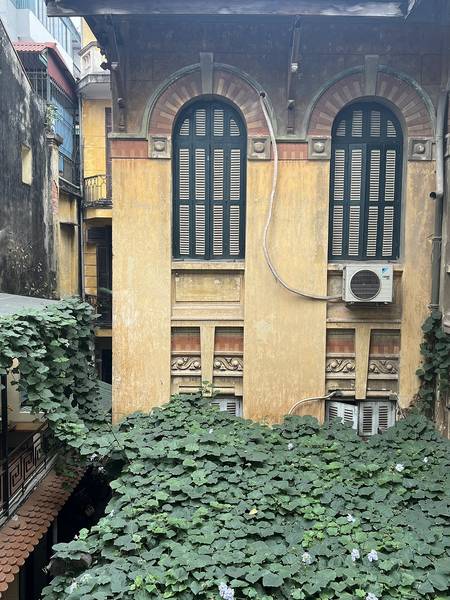 T&ograve;a nh&agrave; cổ với cửa sổ v&ograve;m, điều h&ograve;a b&ecirc;n ngo&agrave;i v&agrave; d&acirc;y leo xanh phủ k&iacute;n s&acirc;n, tạo cảm gi&aacute;c cổ k&iacute;nh v&agrave; tự nhi&ecirc;n.