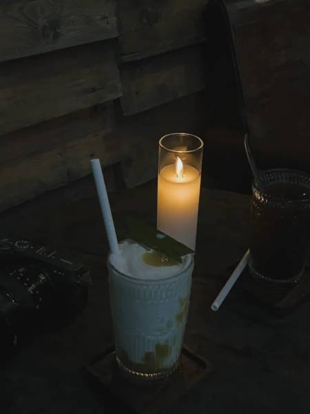 Ly đồ uống với ống h&uacute;t tr&ecirc;n b&agrave;n gỗ, b&ecirc;n cạnh l&agrave; ngọn nến s&aacute;ng trong ly thủy tinh.