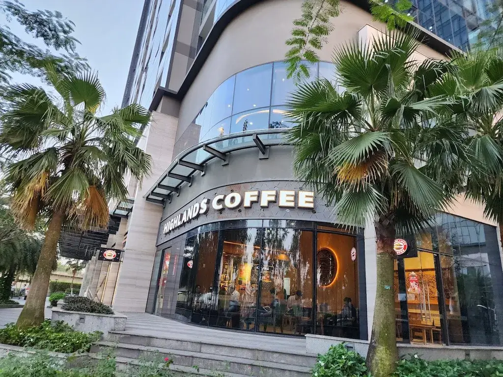 Mặt tiền quán Highlands Coffee với cây cọ trước cửa, tòa nhà hiện đại, không gian trong ánh sáng dịu.