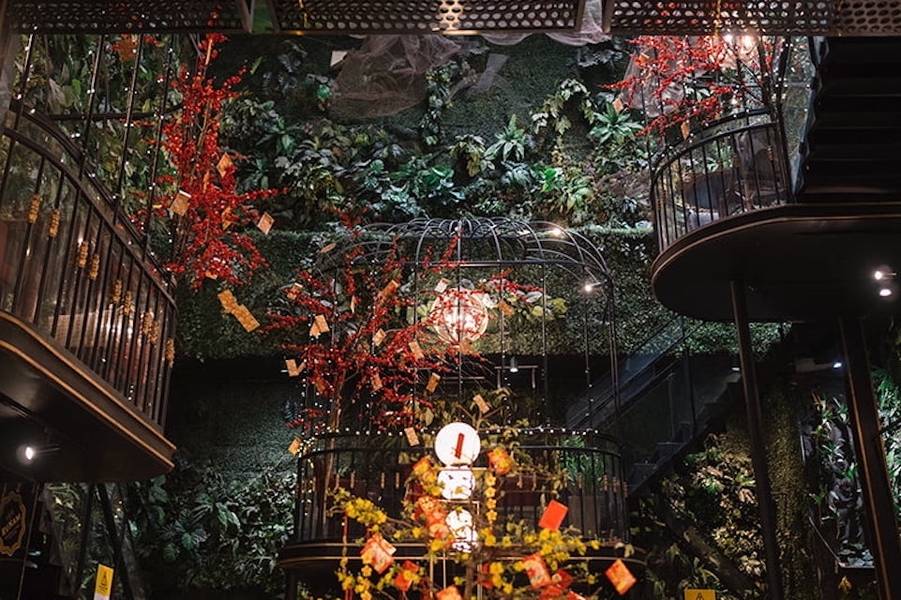 Kh&ocirc;ng gian trang tr&iacute; với c&acirc;y xanh, hoa đỏ v&agrave; lồng đ&egrave;n, tạo cảm gi&aacute;c ấm c&uacute;ng v&agrave; thi&ecirc;n nhi&ecirc;n.