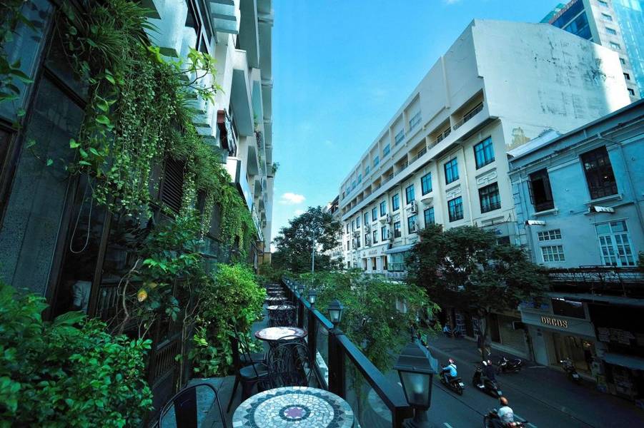 Đường phố với t&ograve;a nh&agrave;, c&acirc;y xanh v&agrave; b&agrave;n ghế ngo&agrave;i trời dưới bầu trời trong xanh.