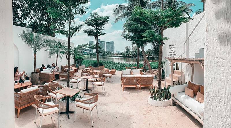 Qu&aacute;n c&agrave; ph&ecirc; ngo&agrave;i trời với b&agrave;n ghế gỗ, c&acirc;y xanh v&agrave; hồ nước, khung cảnh tho&aacute;ng đ&atilde;ng v&agrave; thư gi&atilde;n.