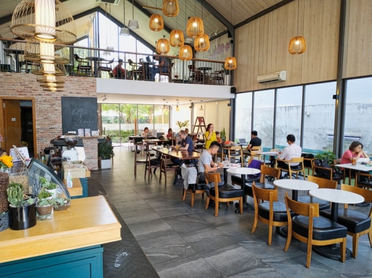 Qu&aacute;n c&agrave; ph&ecirc; c&oacute; trần cao, nhiều b&agrave;n ghế gỗ, đ&egrave;n treo trang tr&iacute; v&agrave; kh&aacute;ch ngồi thư gi&atilde;n, l&agrave;m việc.