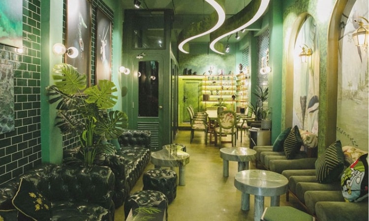 Qu&aacute;n c&agrave; ph&ecirc; trang tr&iacute; t&ocirc;ng m&agrave;u xanh l&aacute;, nội thất hiện đại với ghế sofa v&agrave; b&agrave;n tr&ograve;n, &aacute;nh s&aacute;ng dịu nhẹ.