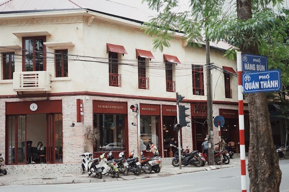 Khám Phá Top 10+ Quán Cafe Quán Thánh Lý Tưởng cho Hẹn Hò, Làm Việc và Thư Giãn 21 Tòa nhà góc phố với quán cà phê ở tầng trệt, có nhiều xe máy đậu phía trước và biển tên đường.