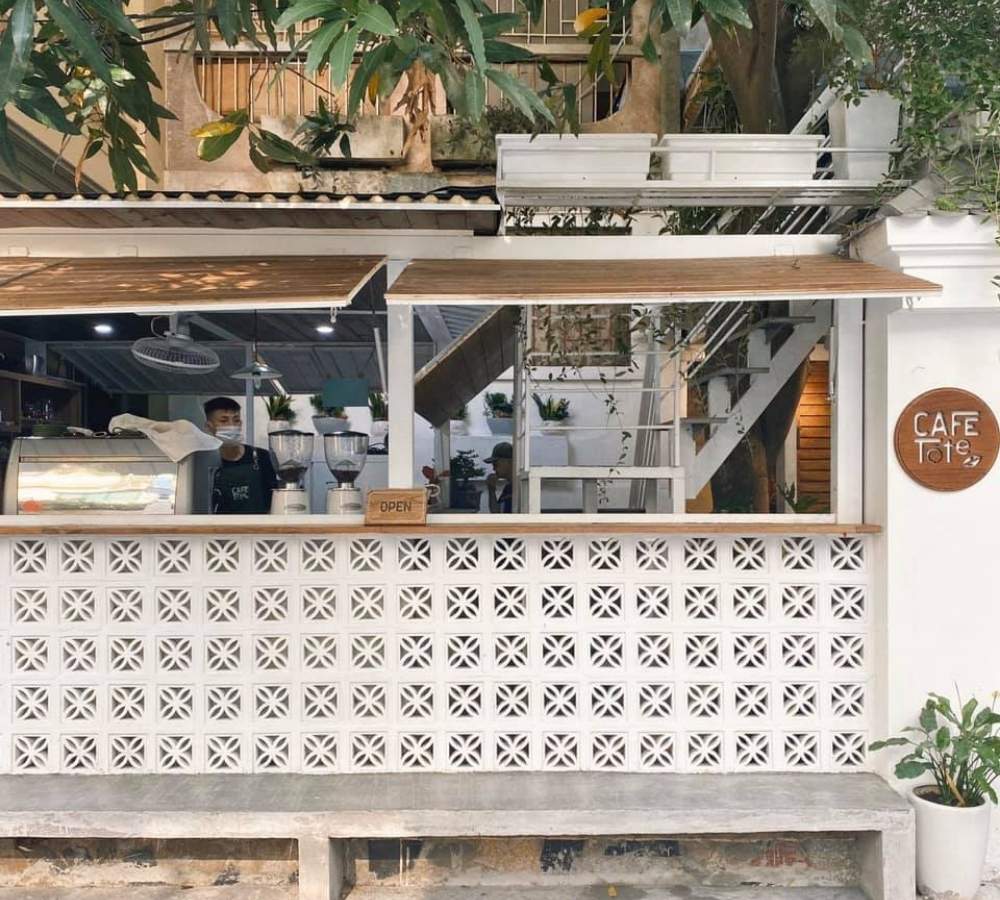 Khám Phá Top Quán Cafe Đẹp Ở Liễu Giai: Đồ Uống Ngon, Không Gian Thư Giãn 7 Quán cà phê với thiết kế mở, có quầy phục vụ bên ngoài và cây xanh xung quanh, phong cách hiện đại và thoáng đãng.