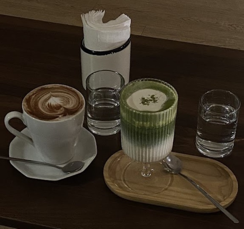 Khám Phá Top 10 Quán Cafe Giảng Võ Hấp Dẫn Nhất Tại Hà Nội 22 Hai ly nước trên bàn, một ly cà phê và một ly trà xanh, kèm theo nước lọc và hộp đựng khăn giấy.