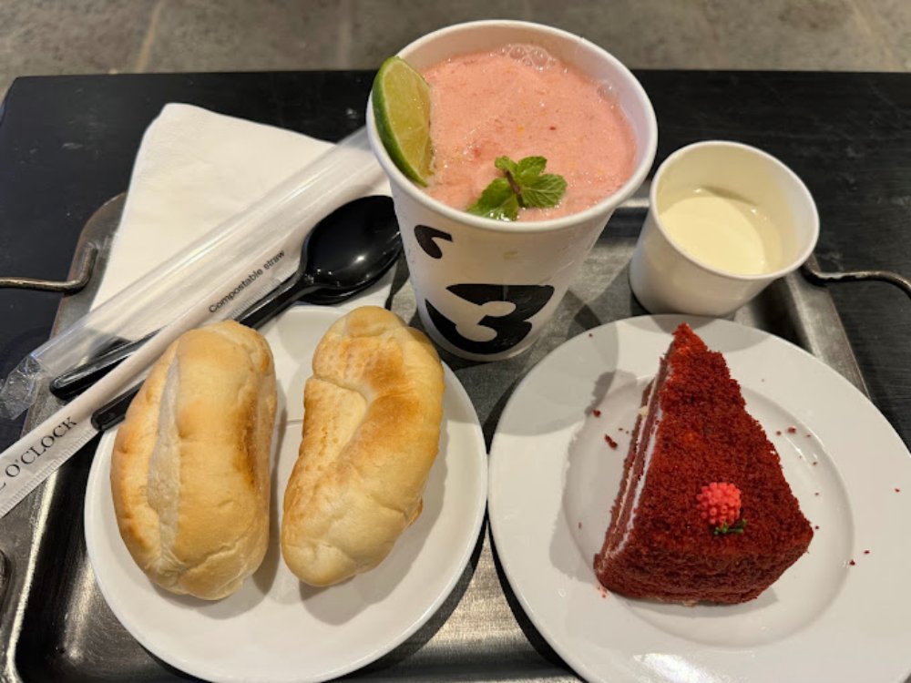 Khám Phá Top 6 Quán Cafe Mở Cửa 24h Tại Quận 3 Cho Người Yêu Thích Cú Đêm 11 Khay đồ ăn gồm bánh mì, bánh ngọt màu đỏ, đồ uống màu hồng và một cốc nhỏ trên bàn.