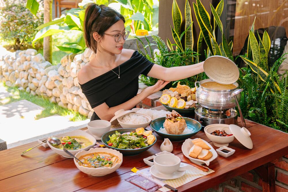 Top 5 Quán Cafe Cá Koi Đẹp Không Thể Bỏ Qua Tại Quy Nhơn 9 Người phụ nữ ngồi bên bàn ăn ngoài trời với nhiều món ăn Việt Nam và cây xanh xung quanh.