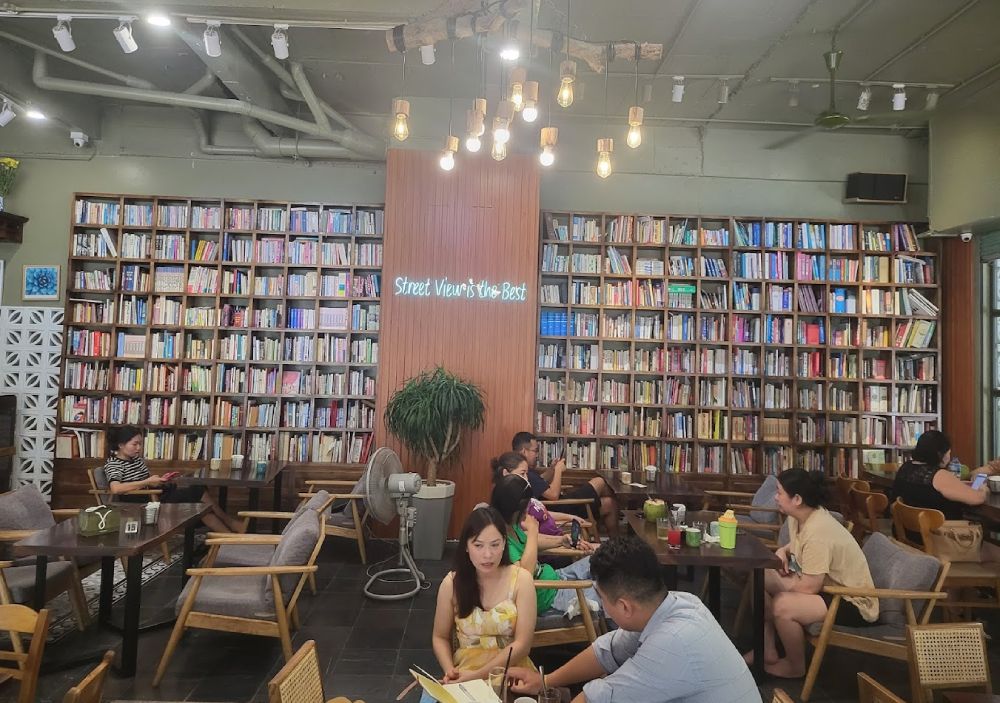 Khám Phá 11 Quán Cafe Sách Độc Đáo Tại Cầu Giấy Hút Hồn Độc Giả 9 Quán cà phê với kệ sách lớn, nhiều người ngồi thư giãn và đọc sách trong không gian ấm cúng.