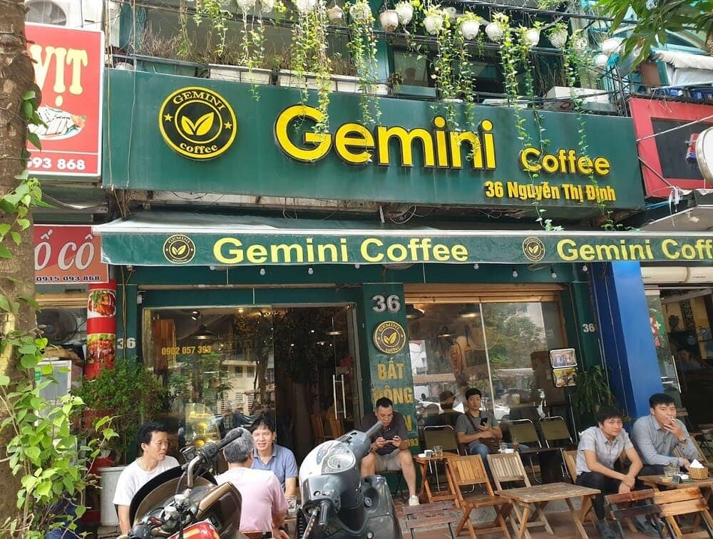 Khám Phá 15 Quán Cafe Hấp Dẫn Trên Đường Nguyễn Thị Định 6 Mặt tiền quán cà phê với bảng hiệu "Gemini Coffee", có khách ngồi bên ngoài và cây xanh trang trí.