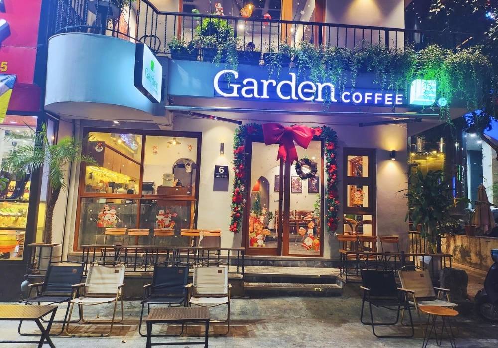 Khám Phá Top Quán Cafe Đẹp Ở Liễu Giai: Đồ Uống Ngon, Không Gian Thư Giãn 13 Quán cà phê trang trí Giáng sinh với vòng hoa và nơ đỏ trên cửa, ghế ngồi ngoài trời, ánh sáng ấm áp.