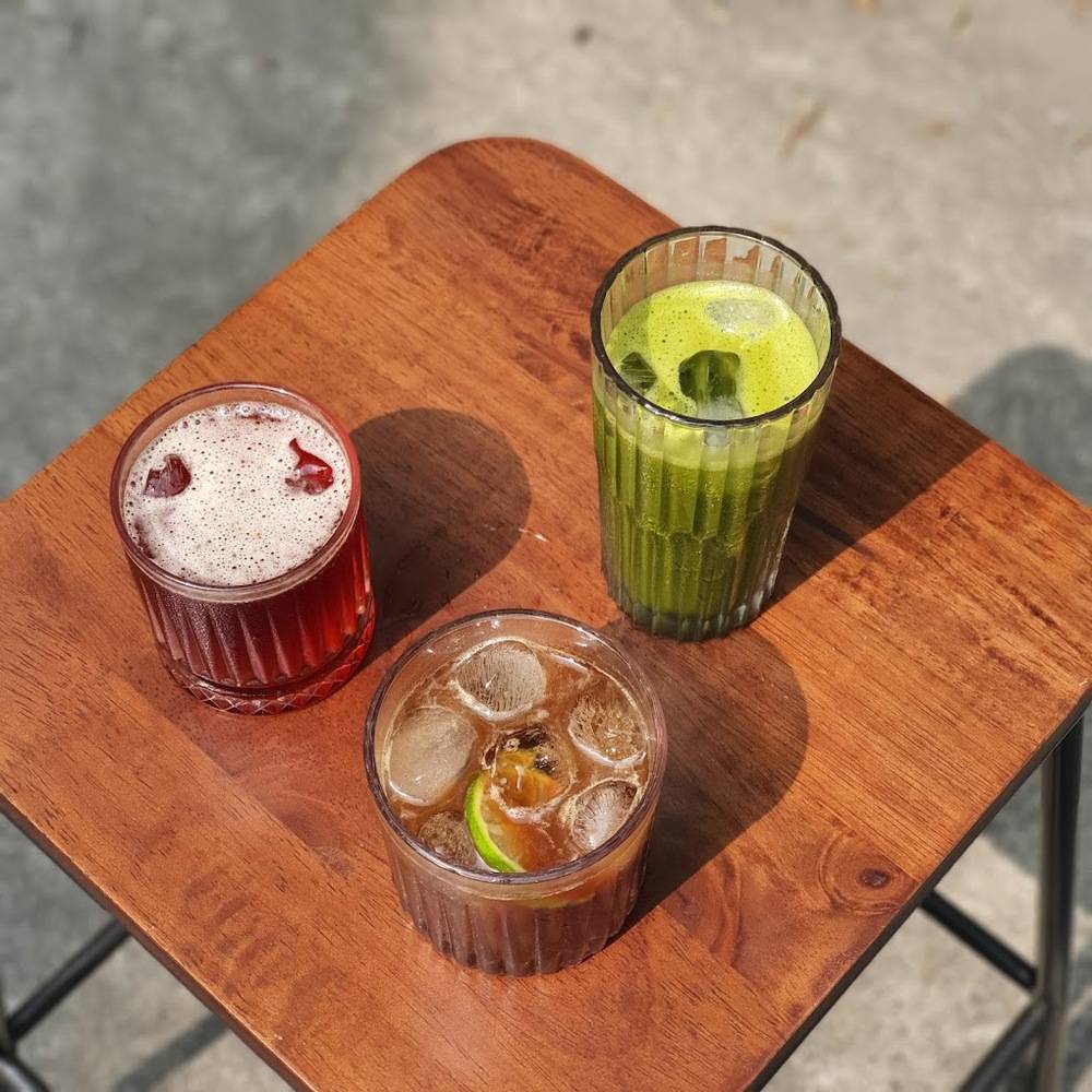 Khám Phá 10+ Quán Cafe Đẹp Ở Đặng Văn Ngữ: Đồ Uống Ngon, Giá Cả Hấp Dẫn 12 Ba ly nước đa dạng màu sắc đặt trên bàn gỗ, bao gồm nước đỏ, nước xanh và nước nâu với đá.