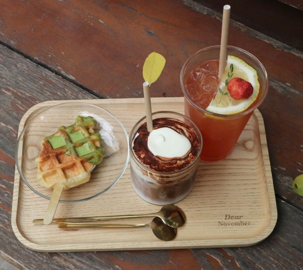 15 Quán Cafe Chùa Láng Với Không Gian Thư Giãn Tuyệt Đẹp 9 Khây gỗ với ly trà, bánh waffle que và ly cà phê kem tươi, đặt trên bàn gỗ.