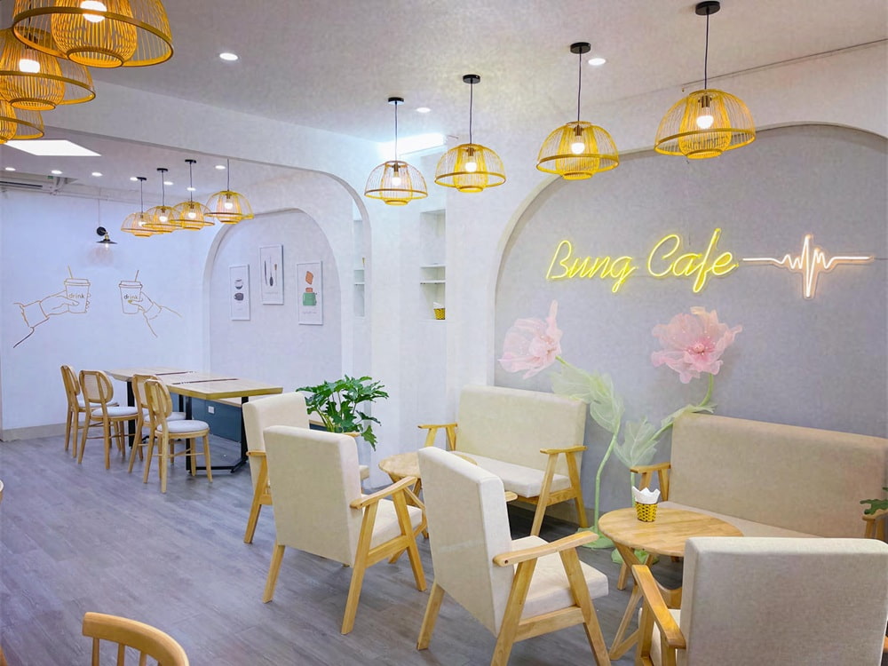 15 Quán Cafe Chùa Láng Với Không Gian Thư Giãn Tuyệt Đẹp 21 Quán cà phê trang trí hiện đại với bàn ghế gỗ, đèn treo và chữ neon sáng trên tường, không gian thoáng đãng.