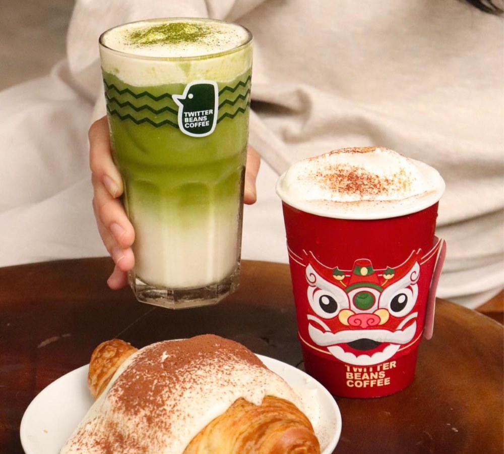 Khám Phá Top 10 Quán Cafe Giảng Võ Hấp Dẫn Nhất Tại Hà Nội 4 Một ly matcha latte, một cốc cà phê có họa tiết đỏ và một chiếc bánh sừng bò trên bàn.