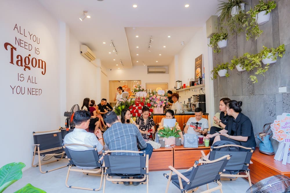 Khám Phá 15 Quán Cafe Hấp Dẫn Trên Đường Nguyễn Thị Định 15 Nhóm người ngồi trò chuyện trong quán cà phê hiện đại, tường trang trí cây xanh và chữ nghệ thuật.