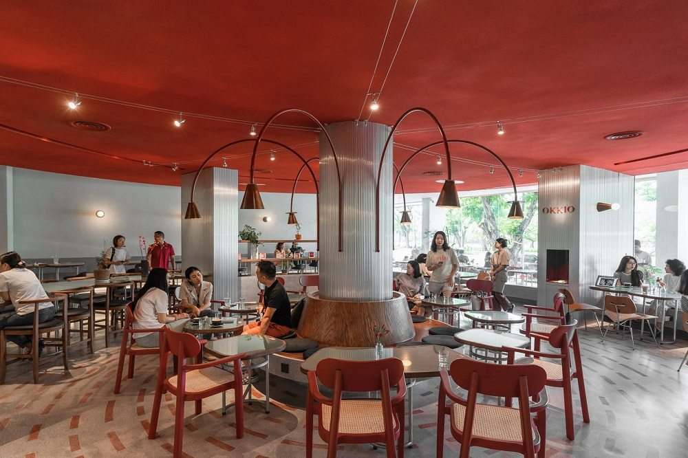 Khám Phá Những Quán Cafe Độc Lạ Thu Hút Giới Trẻ Tại Sài Gòn 21 Quán cà phê hiện đại với trần đỏ, đèn treo và khách ngồi trò chuyện tại các bàn ghế gỗ, không gian sáng sủa.