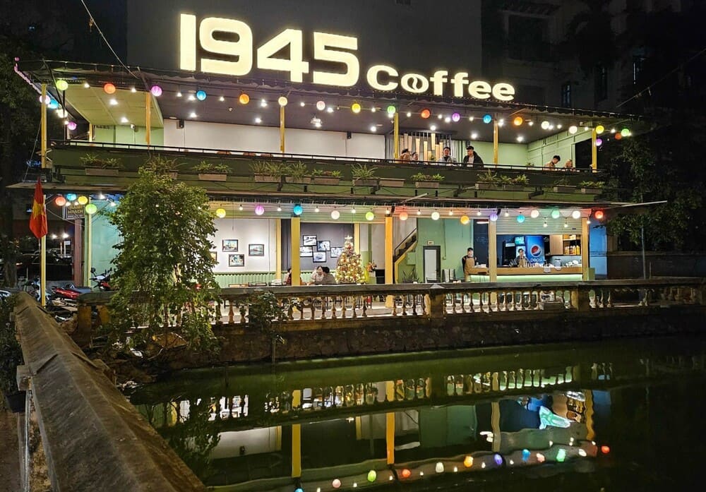 Khám Phá 15 Quán Cafe Hấp Dẫn Trên Đường Nguyễn Thị Định 4 Quán cà phê hai tầng, bảng hiệu "1945 Coffee", trang trí đèn lồng nhiều màu, có cây xanh và hồ nước phía trước.