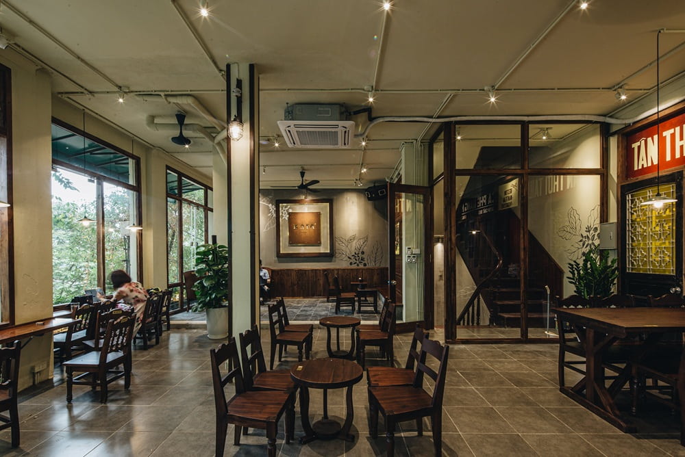 Khám Phá 15+ Quán Cafe View Đẹp, Đồ Uống Ngon Tại Hoàng Cầu 13 Quán cà phê với bàn ghế gỗ, ánh sáng ấm áp, cửa sổ lớn nhìn ra cây xanh, không gian thoáng đãng và hiện đại.