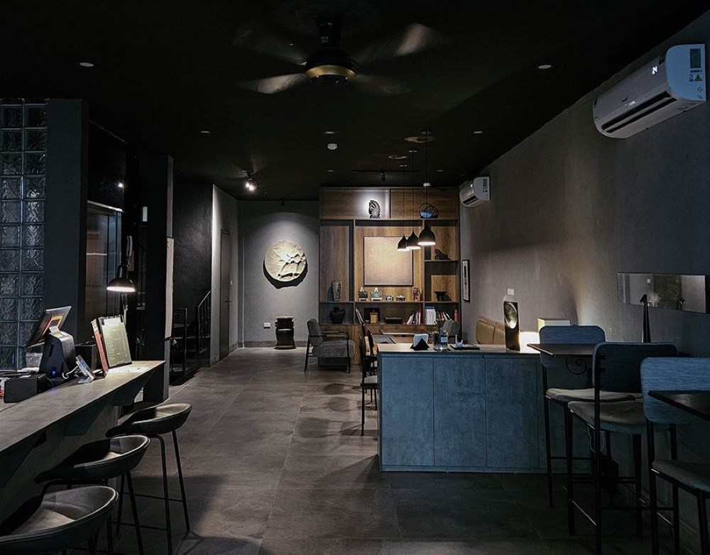 Khám Phá Top 10 Quán Cafe Giảng Võ Hấp Dẫn Nhất Tại Hà Nội 15 Không gian nội thất tối giản với bàn ghế và đồ trang trí, ánh sáng nhẹ từ đèn trần và đèn bàn.
