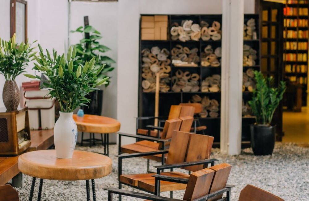 Khám Phá 9 Quán Cafe Độc Đáo Trên Đường Hoàng Hoa Thám 6 Không gian nội thất ấm cúng với bàn ghế gỗ, bình hoa trang trí, kệ sách và cây xanh.