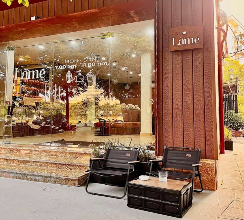 15 Quán Cafe Chùa Láng Với Không Gian Thư Giãn Tuyệt Đẹp 19 Mặt tiền quán cà phê với cửa kính lớn, bảng hiệu gỗ và hai ghế ngồi cạnh bàn nhỏ ngoài trời.