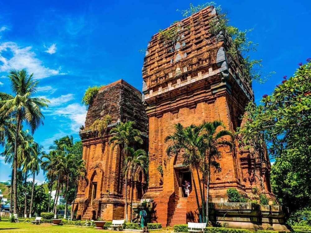 Top 5 Quán Cafe Cá Koi Đẹp Không Thể Bỏ Qua Tại Quy Nhơn 13 Tháp gạch cổ giữa hàng cây xanh, trời xanh nắng đẹp, người đứng trong tháp, khung cảnh yên bình.