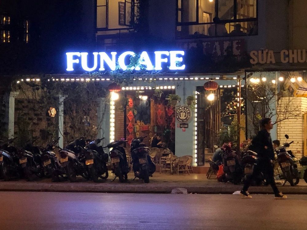 Khám Phá 10+ Quán Cafe Đẹp Ở Đặng Văn Ngữ: Đồ Uống Ngon, Giá Cả Hấp Dẫn 7 Quán cà phê với biển hiệu sáng đèn, nhiều xe máy đỗ trước cửa, một người đi bộ ngang qua.