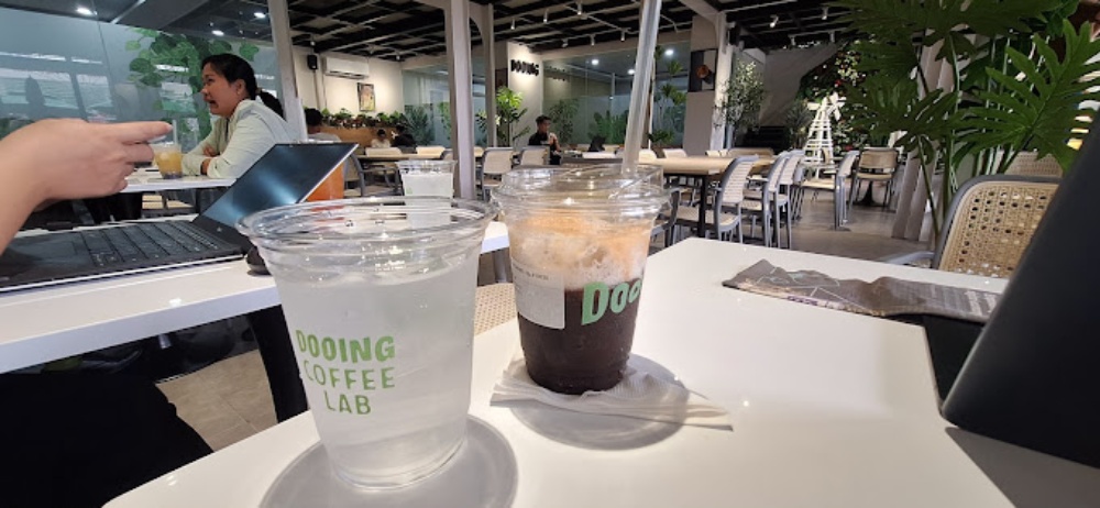 Khám Phá Top 6 Quán Cafe Mở Cửa 24h Tại Quận 3 Cho Người Yêu Thích Cú Đêm 20 Hai ly nước trên bàn trong quán cà phê hiện đại, phía sau có người đang ngồi làm việc với laptop.