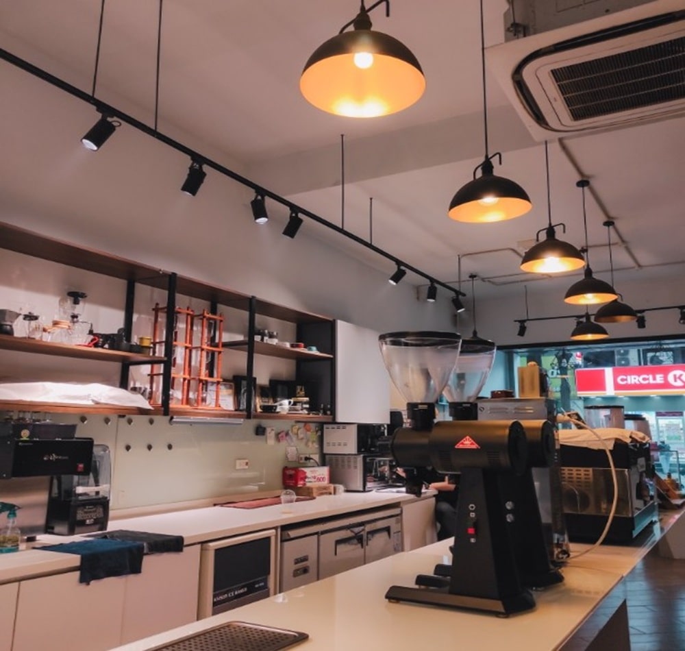 15 Quán Cafe Chùa Láng Với Không Gian Thư Giãn Tuyệt Đẹp 14 Quán cà phê hiện đại với máy pha cà phê trên quầy và ánh sáng từ đèn trần.