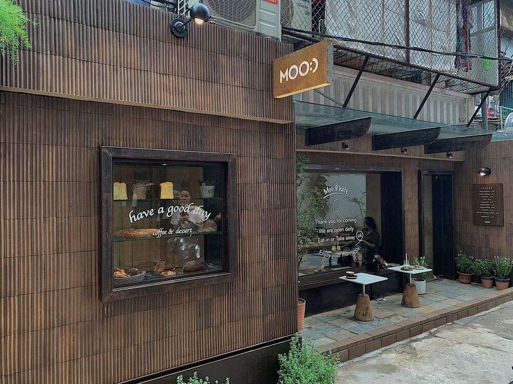 Khám Phá 10+ Quán Cafe Đẹp Ở Đặng Văn Ngữ: Đồ Uống Ngon, Giá Cả Hấp Dẫn 27 Mặt tiền quán cà phê với biển hiệu "MOO:D", cửa sổ trưng bày bánh ngọt và bàn ngoài trời.