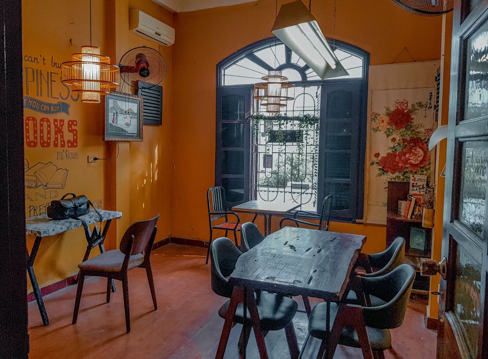 Khám Phá 11 Quán Cafe Sách Độc Đáo Tại Cầu Giấy Hút Hồn Độc Giả 14 Căn phòng ấm cúng với bàn ghế gỗ, cửa sổ lớn, ánh sáng tự nhiên, tranh tường và đèn trang trí.