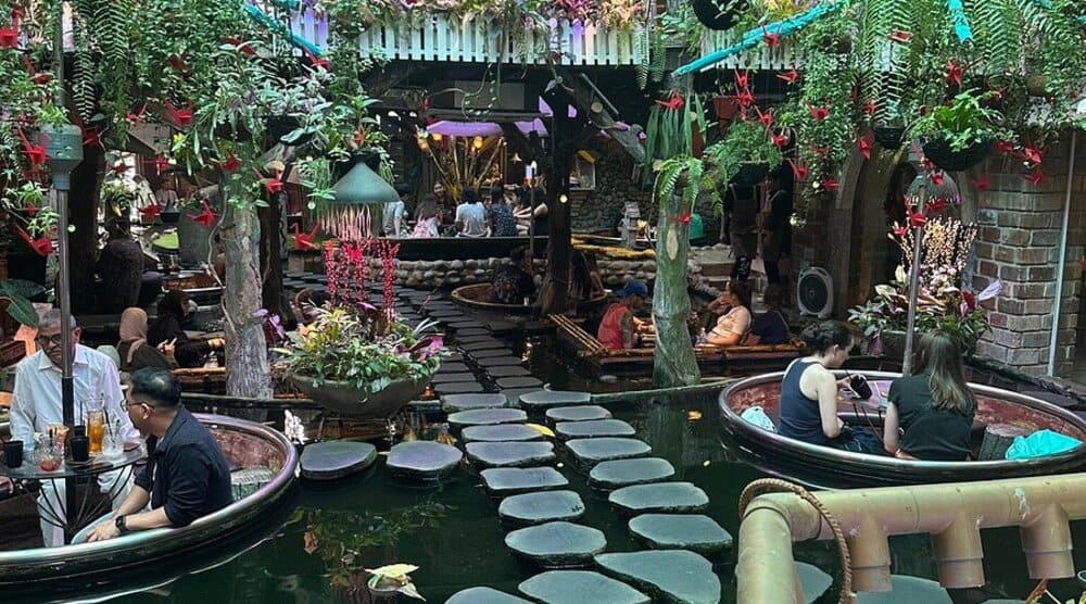 Quán cà phê trang trí cây xanh, bàn ngồi trong thuyền tròn trên nước, lối đi bằng đá.