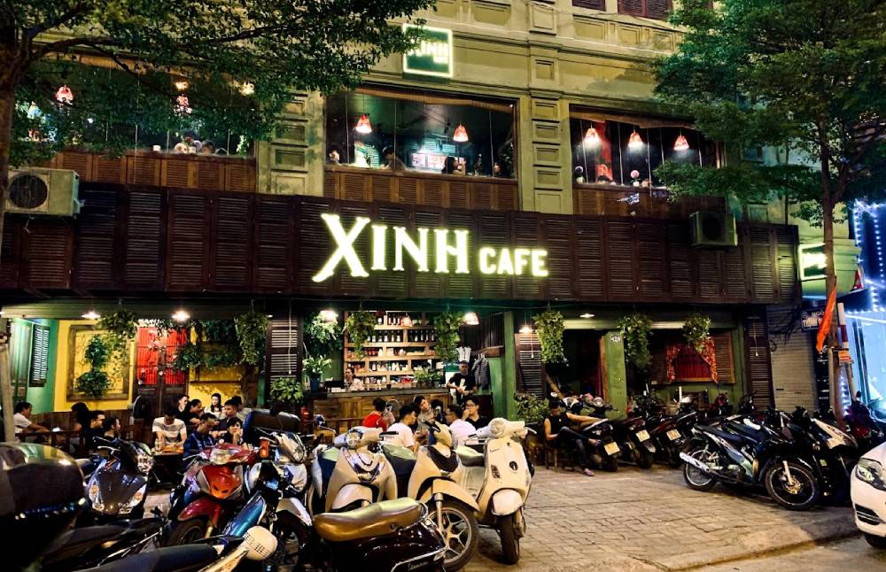 Khám Phá 12+ Quán Cafe Đẹp Ở Tây Sơn Với Đồ Uống Ngon 14 Quán cà phê đông đúc vào buổi tối, nhiều người ngồi trước quán, xe máy đỗ kín vỉa hè, ánh sáng ấm áp.