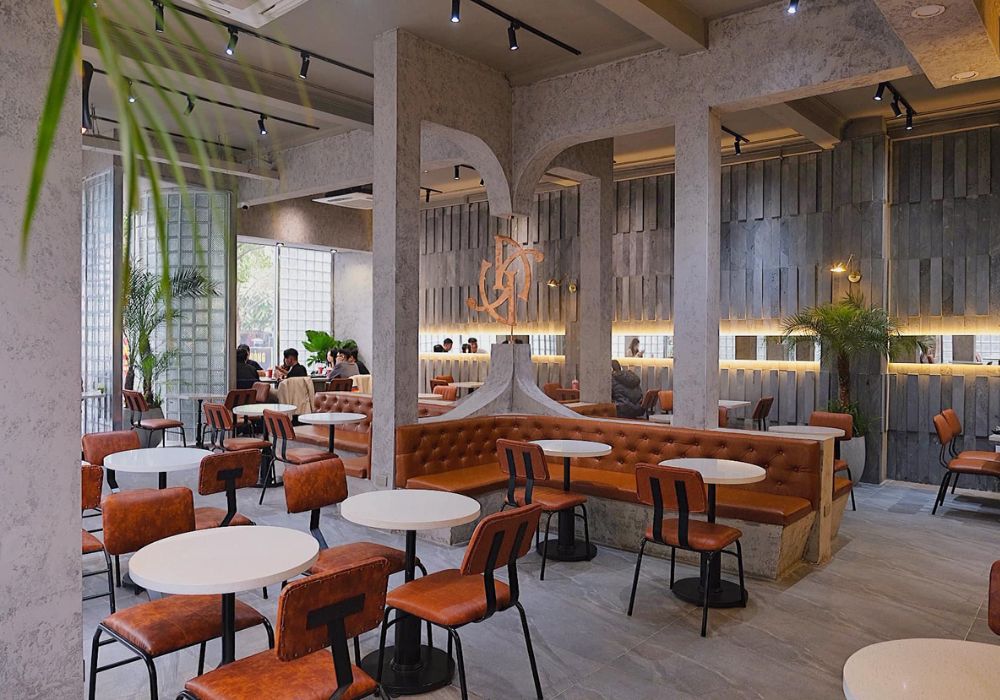 Khám Phá Top 10 Quán Cafe Láng Hạ: View Đẹp, Menu Hấp Dẫn, Giá Cực Hợp Lý 6 Không gian quán cà phê hiện đại với bàn ghế da màu cam, trang trí cây xanh và ánh sáng ấm áp.