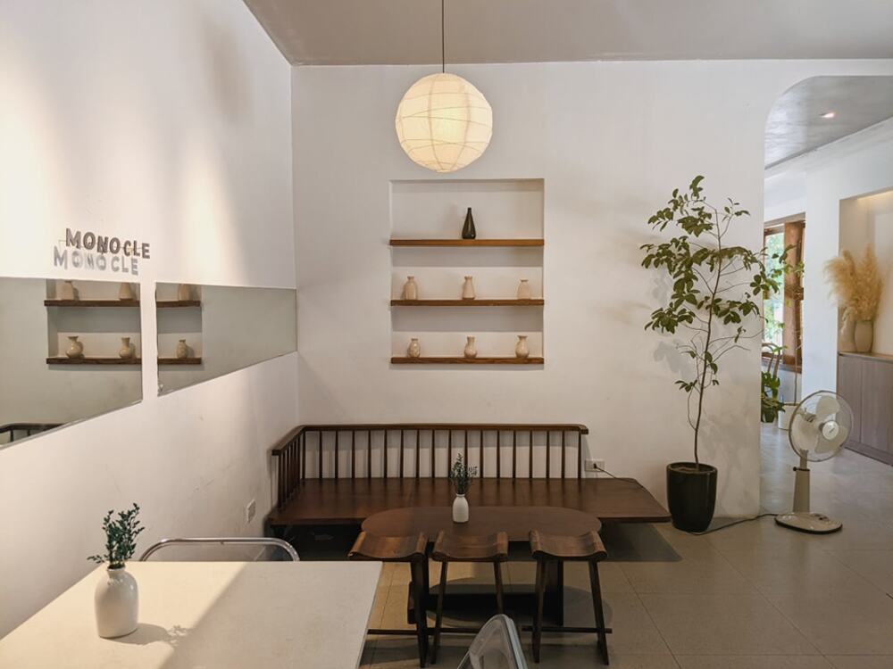 Khám Phá 10+ Quán Cafe Đẹp Ở Đặng Văn Ngữ: Đồ Uống Ngon, Giá Cả Hấp Dẫn 14 Quán cà phê với bàn ghế gỗ, cây xanh, đèn treo và kệ trang trí trên tường trắng.
