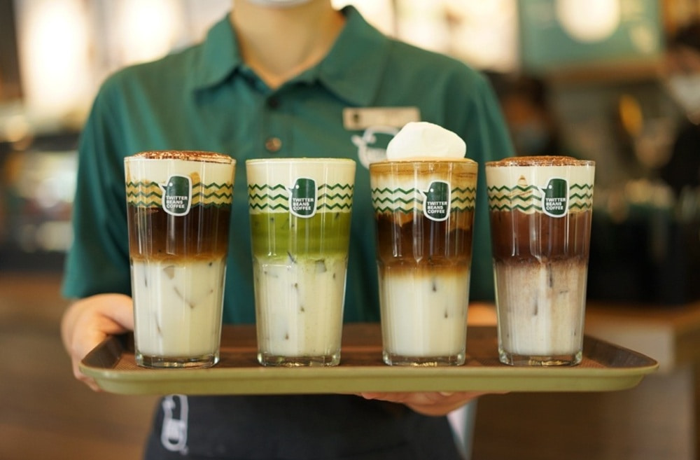 Khám Phá 15+ Quán Cafe View Đẹp, Đồ Uống Ngon Tại Hoàng Cầu 18 Người phục vụ cầm khay có bốn ly cà phê sữa, trang trí đẹp mắt, trong không gian quán cà phê.