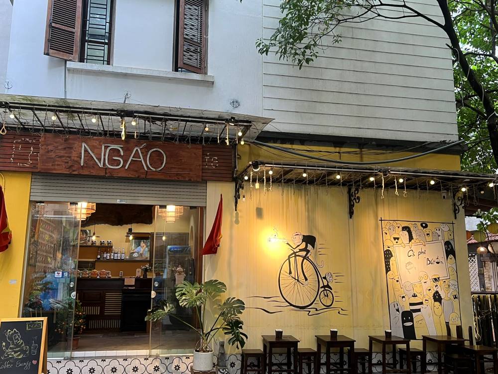 Khám Phá Top 10 Quán Cafe Giảng Võ Hấp Dẫn Nhất Tại Hà Nội 11 Mặt tiền quán cà phê với biển hiệu, tranh tường nghệ thuật và dãy bàn ghế gỗ bên ngoài.