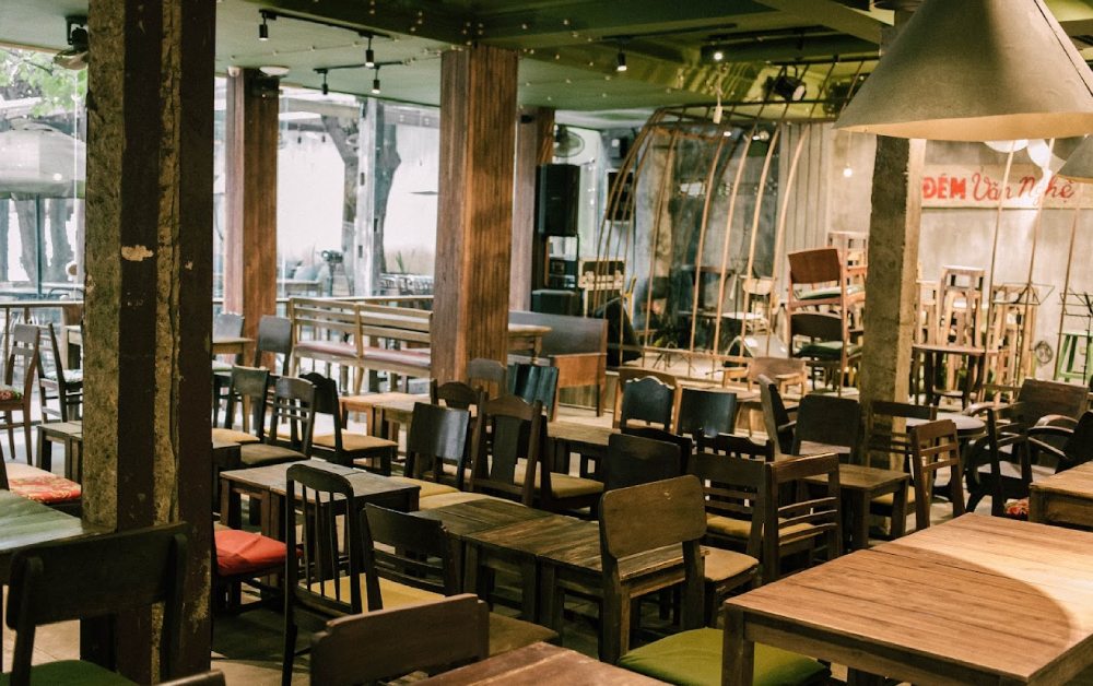 Khám Phá 7 Quán Cafe Tuyệt Đẹp Ở Ngã Tư Sở: View Đẹp, Đồ Uống Ngon, Giá Phải Chăng 7 Quán cà phê với bàn ghế gỗ xếp gọn gàng, ánh sáng nhẹ nhàng, không gian ấm cúng và trang trí độc đáo.