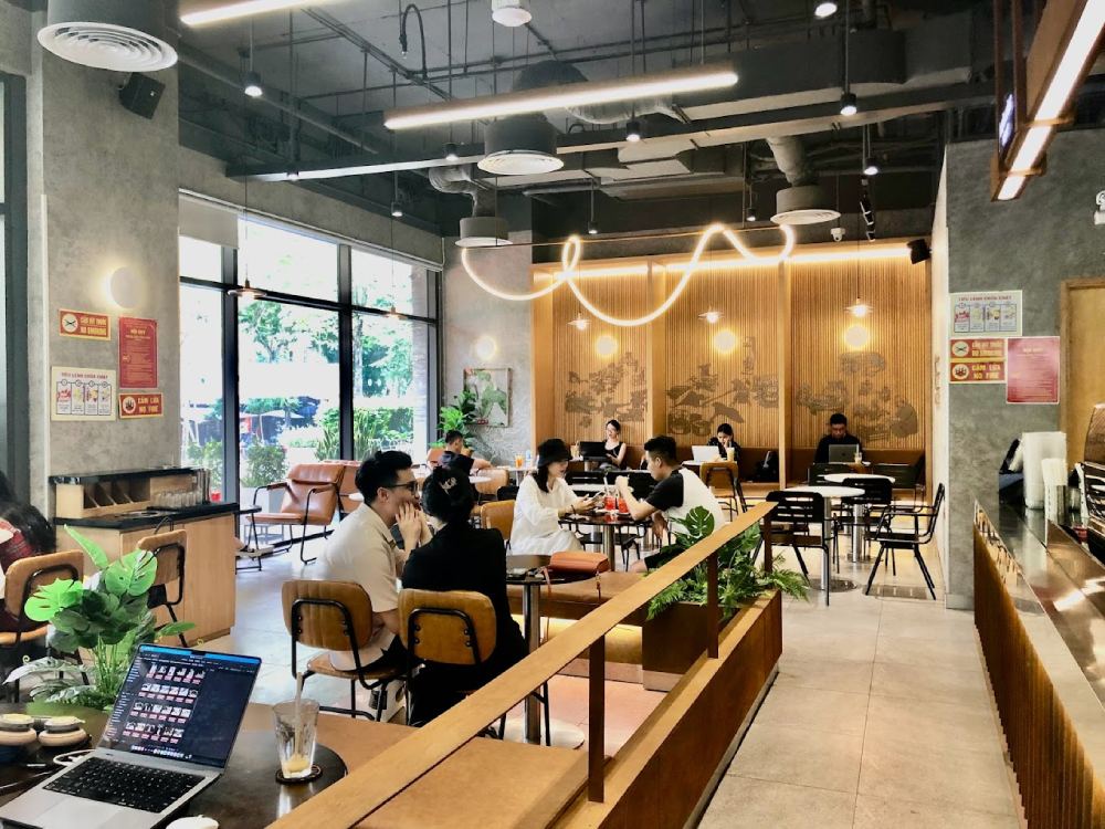 Khám Phá 11 Quán Cafe Đội Cấn Tuyệt Vời Cho Thư Giãn Và Làm Việc 13 Quán cà phê với nhiều người ngồi làm việc và trò chuyện, trang trí hiện đại, ánh sáng ấm áp.